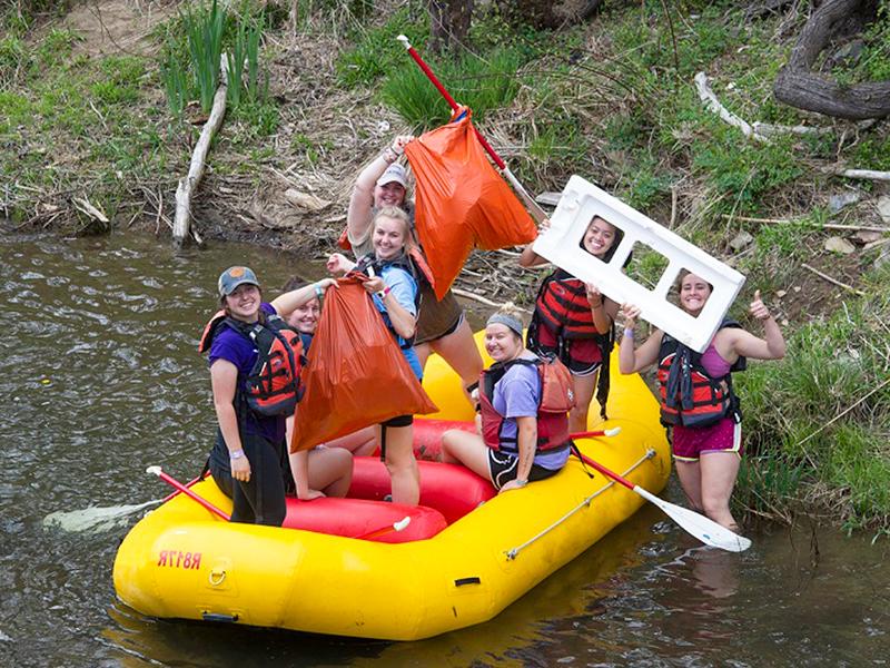 a group of students in a river raft hold up trash they have collected from the river